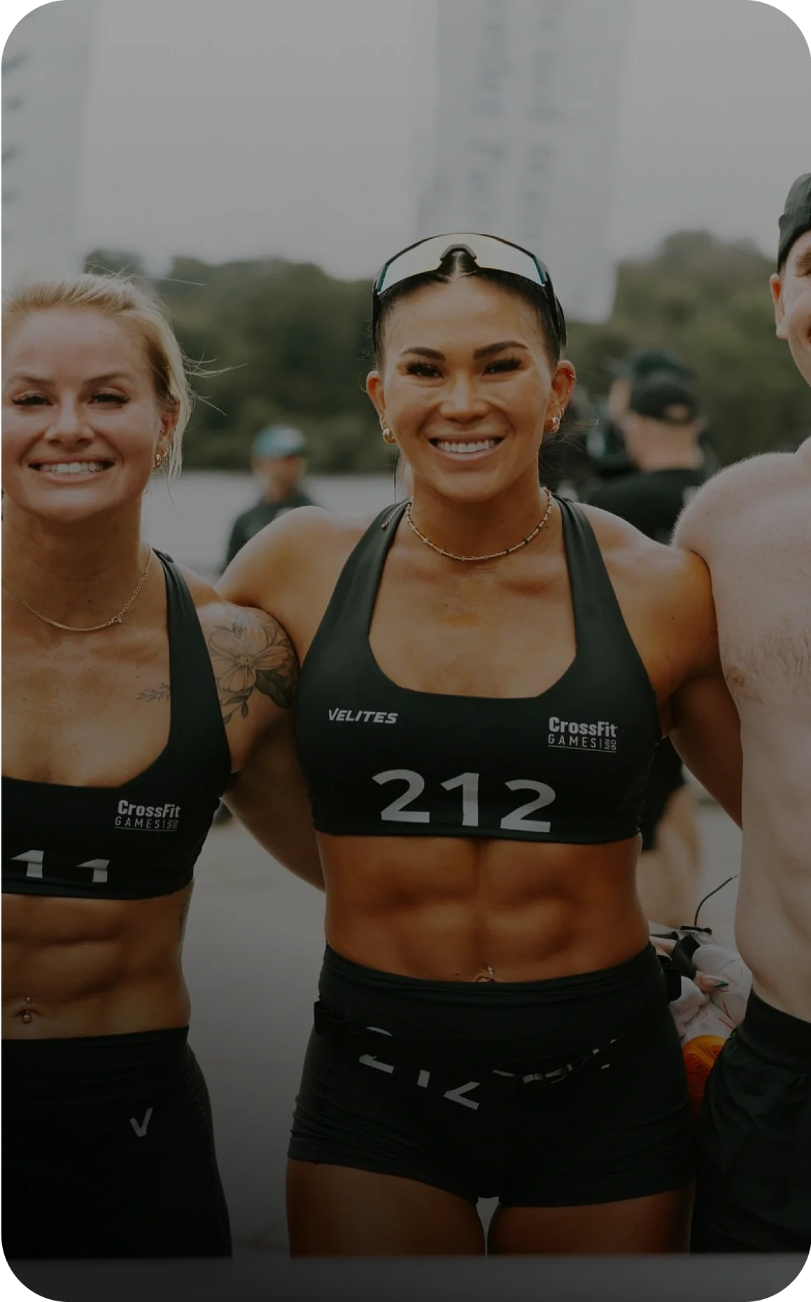 Photo of a woman wearing athletic gear with the number 212, standing alongside other athletes outdoors, labeled as Emily Loogman, T&F All-American, 3x CF Games, Hybrid Athlete.