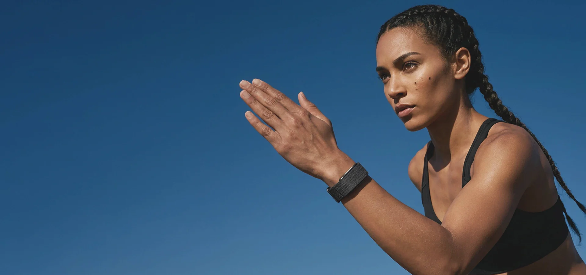 Person wearing a hume band 2.0 while outdoors in an athletic stance against a clear blue sky, appearing focused and ready for exercise or training.